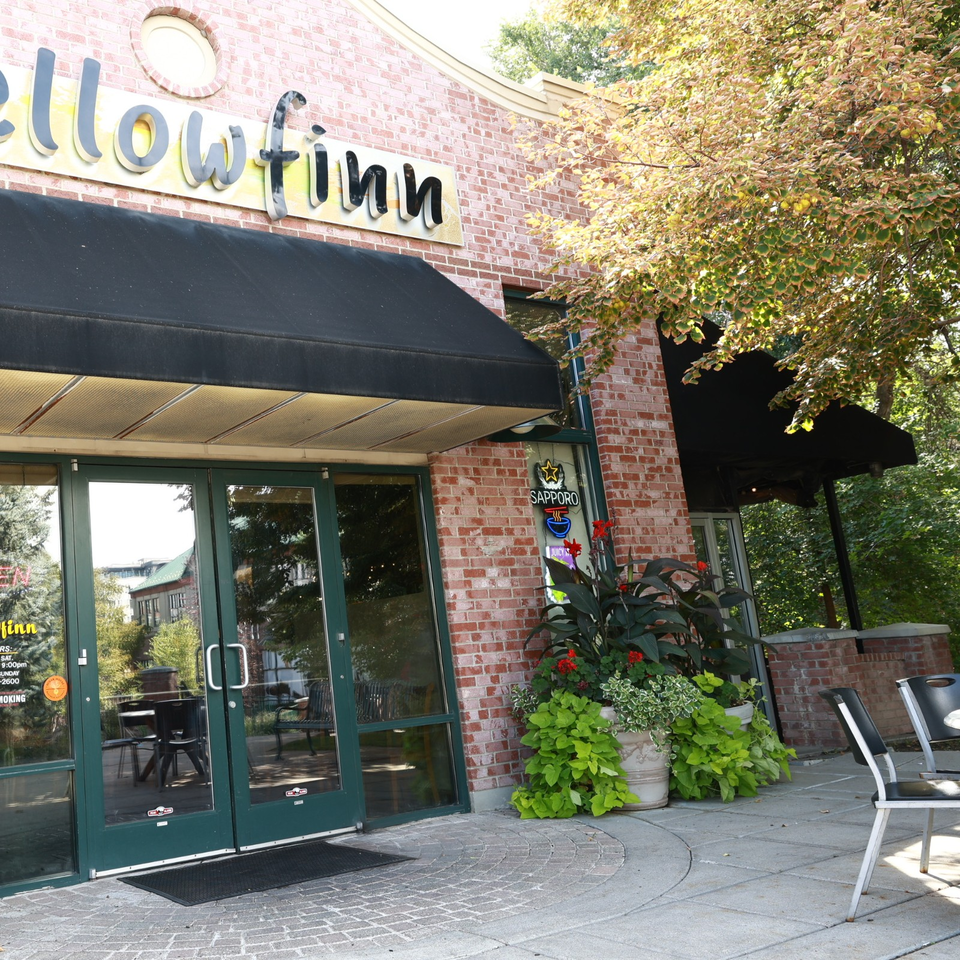 Exterior of Sapporo restaurant with brick walls, black awnings, green doors, outdoor seating, and colorful flower planters.