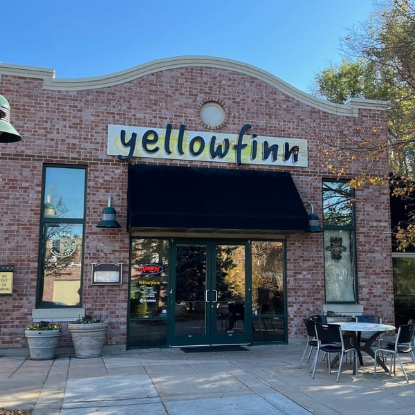 Exterior of Yellowfinn Grill & Sushi Bar, a brick building with a black awning and outdoor seating.
