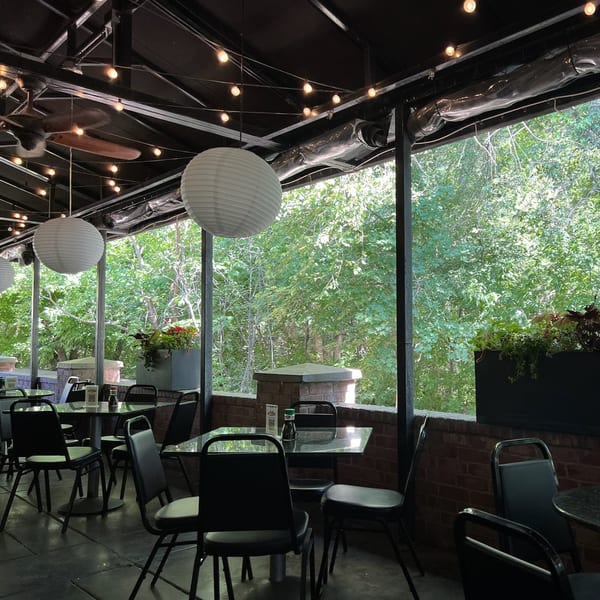 Outdoor patio at Yellowfinn Grill & Sushi Bar with tables, chairs, paper lanterns, and lush greenery.