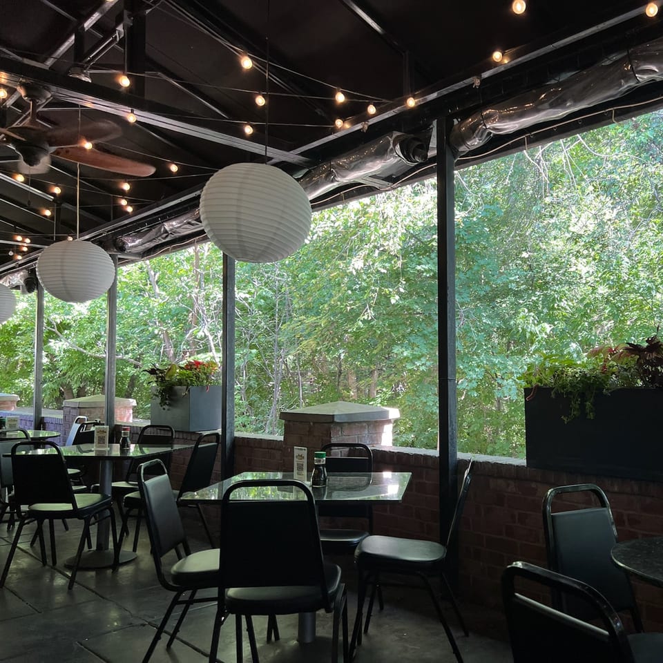 Outdoor patio at Yellowfinn Grill & Sushi Bar with tables, chairs, paper lanterns, and lush greenery.