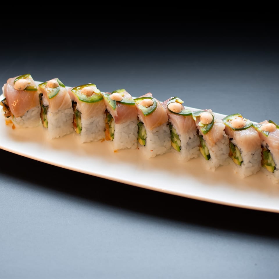 Yellowtail sushi rolls with jalapeño and spicy mayo on a white rectangular plate.