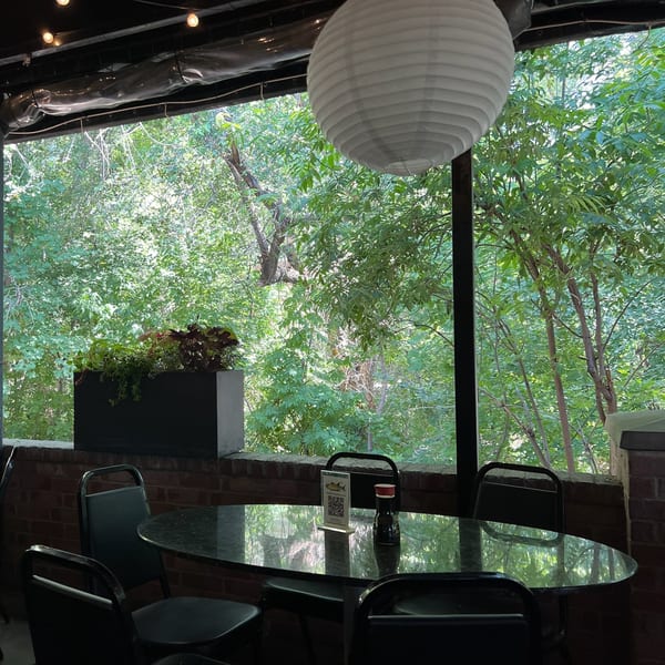 Outdoor dining area at Yellowfinn Grill & Sushi Bar with a table, chairs, and lush green trees.
