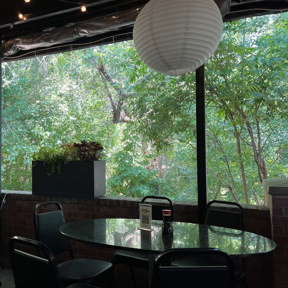 Outdoor dining area at Yellowfinn Grill & Sushi Bar with a table, chairs, and lush green trees.