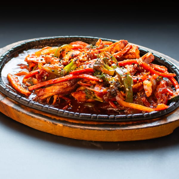 Sizzling stir-fry with chicken, broccoli, and bell peppers, garnished with sesame seeds on a hot plate.