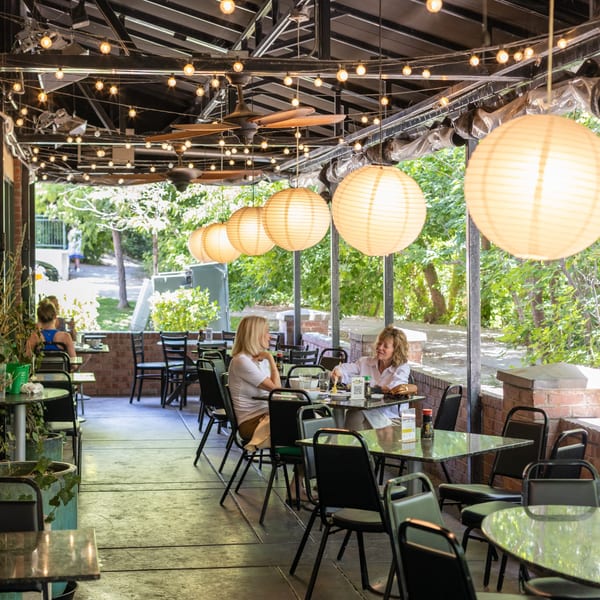 Two women dining on the Yellowfinn Grill & Sushi Bar patio under string lights and paper lanterns.