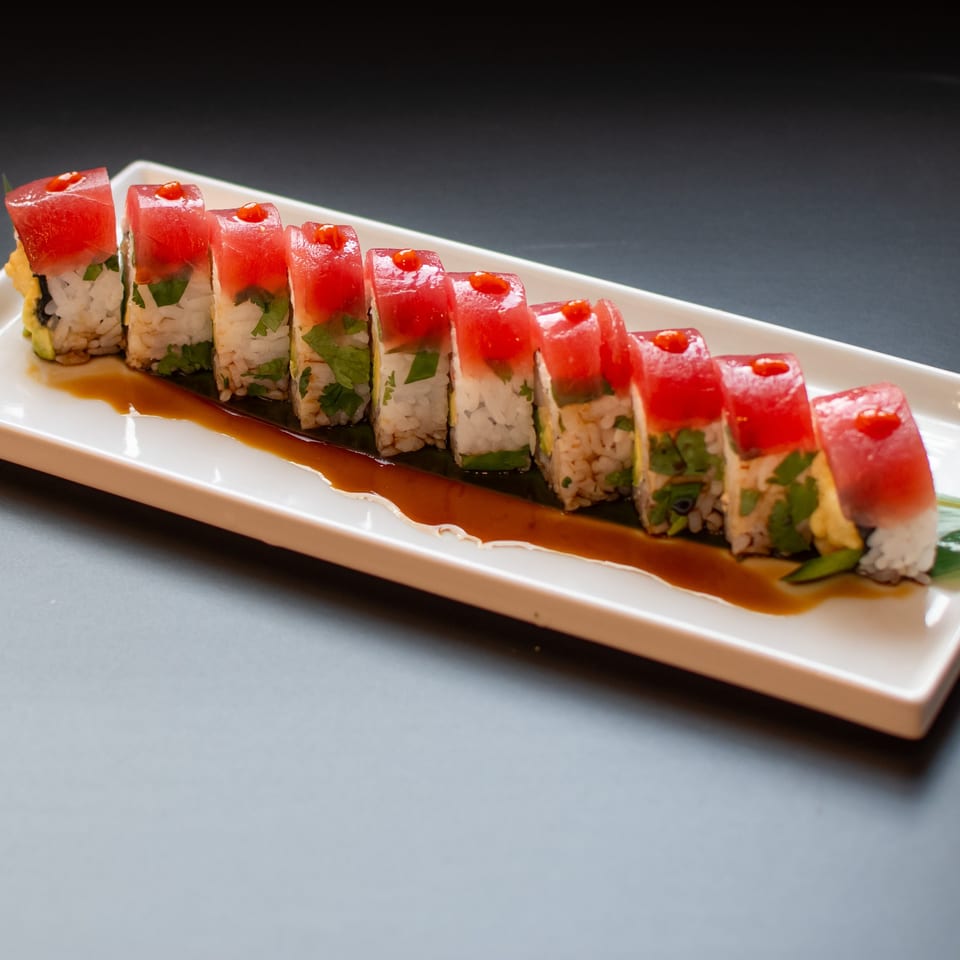 Yellowfinn Grill & Sushi Bar's tuna sushi roll with red sauce drizzle on a white rectangular plate.